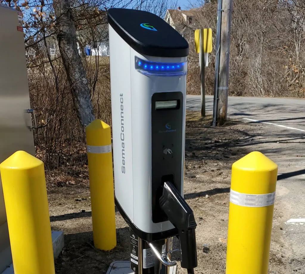 SemaConnect electric vehicle charging station with a charging plug, surrounded by yellow bollards, located in a Massachusetts setting, emphasizing clean energy advancements.