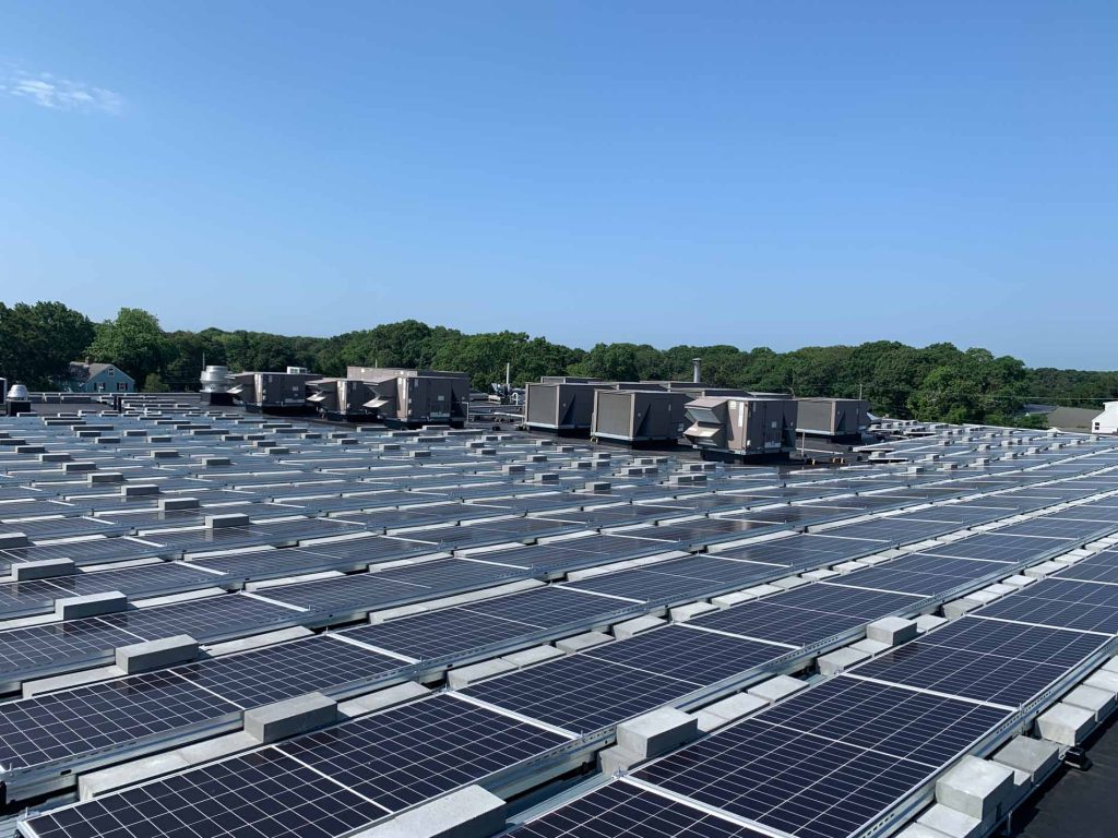 Solar panel installation on a commercial building roof in Cape Cod, MA, showcasing numerous solar panels and HVAC units, emphasizing clean energy solutions for local businesses.