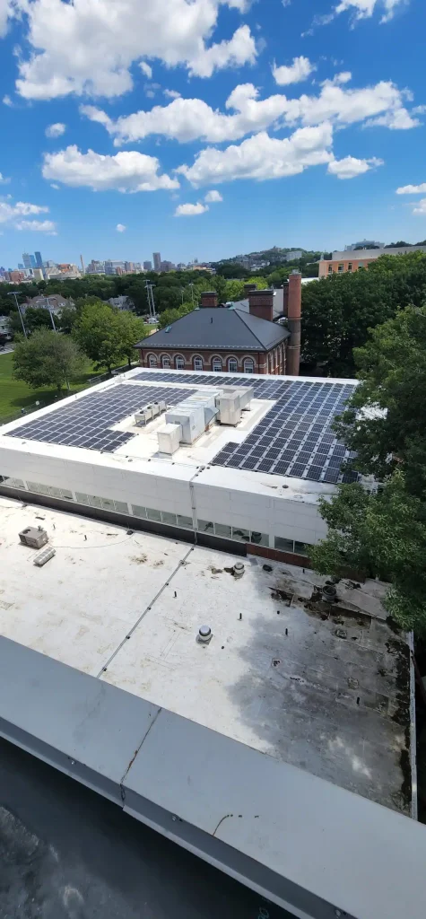 Solar panel installation on the roof of Brookline Kirrane Aquatics Center, showcasing clean energy solutions against a backdrop of blue sky and city skyline.