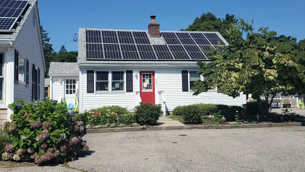 Residential building with solar panels on the roof, surrounded by landscaped garden and clear blue sky, showcasing solar energy solutions for homes.