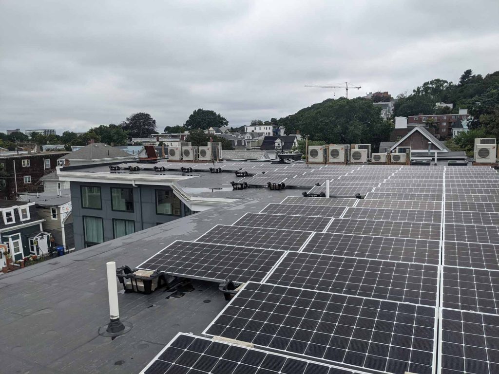 Roof covered with solar panels at Eleanor Lofts, showcasing commercial solar power installation amidst a cityscape with air conditioning units and overcast skies.