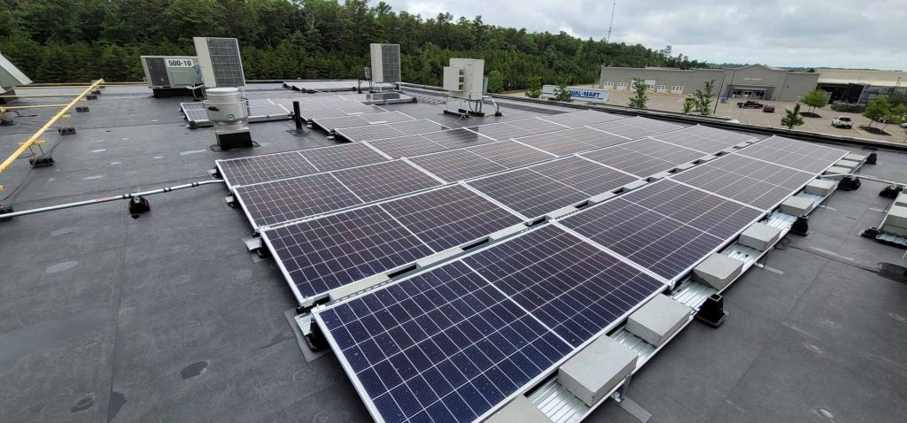 Mazda dealership roof featuring solar panel installation, showcasing multiple solar panels and HVAC units against a backdrop of greenery and commercial buildings, emphasizing clean energy solutions for businesses.