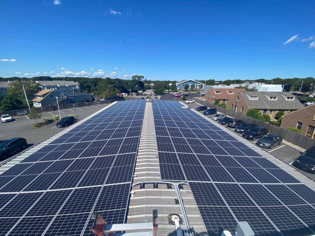 Solar panel installation on a commercial building in Cape Cod, MA, showcasing a large array of solar panels on a rooftop with a clear blue sky and surrounding parking area.