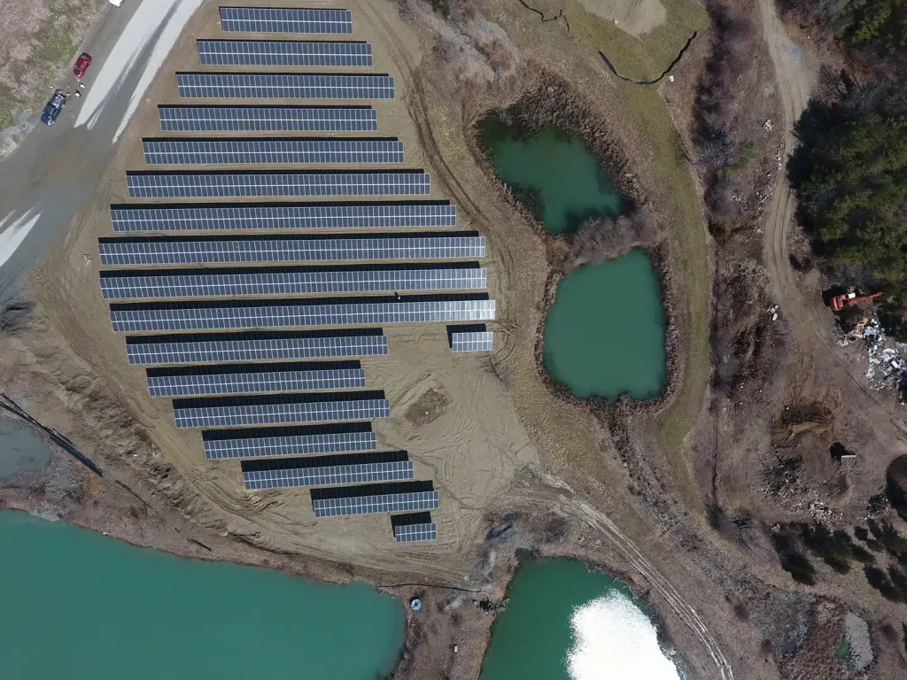 Aerial view of solar ground-mounted panels arranged in rows, surrounded by water bodies and natural landscape, showcasing BD Electrical Services' commitment to commercial solar power installations.